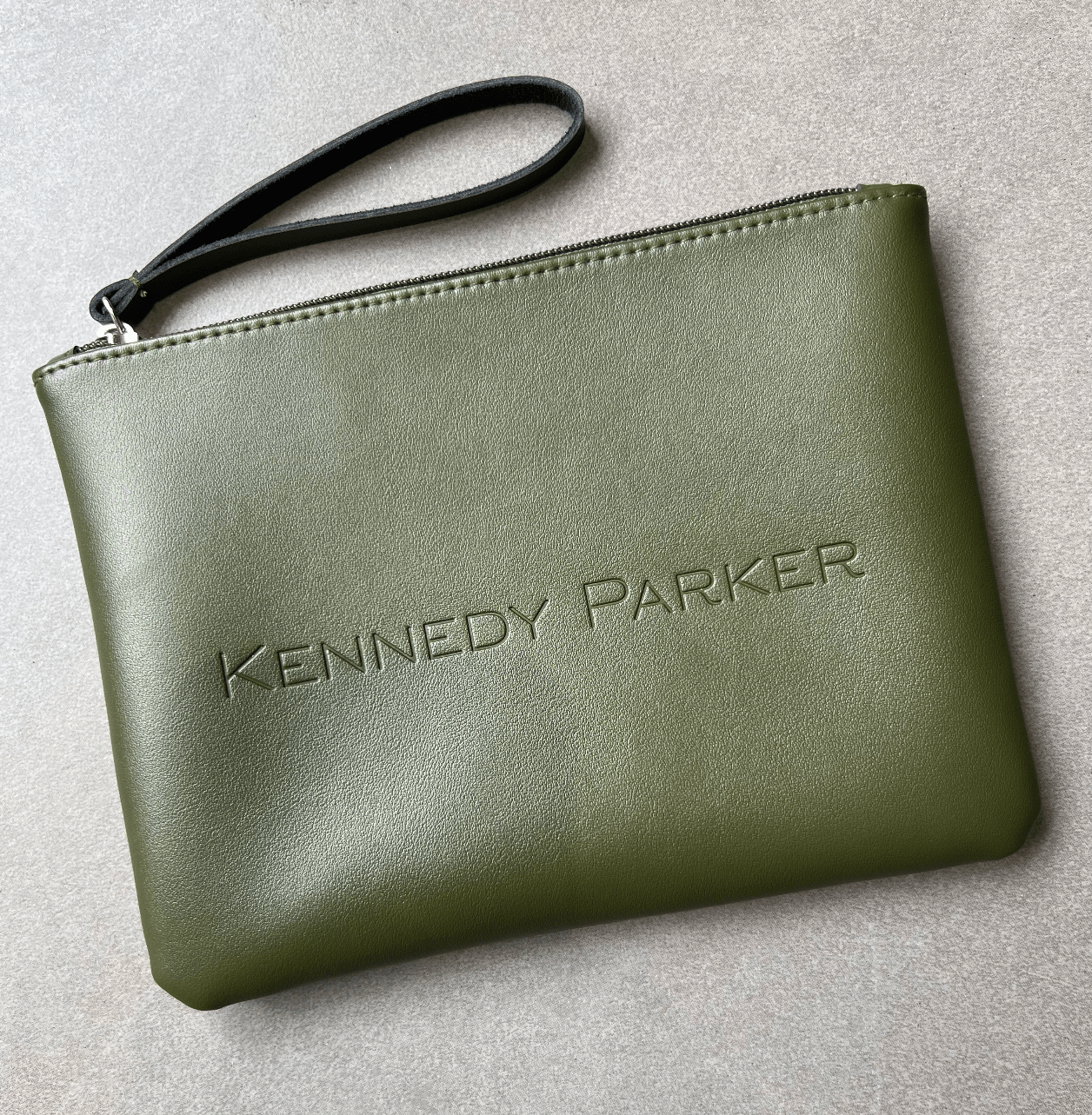 Green clutch bag with 'Kennedy Parker' branding on a light gray background